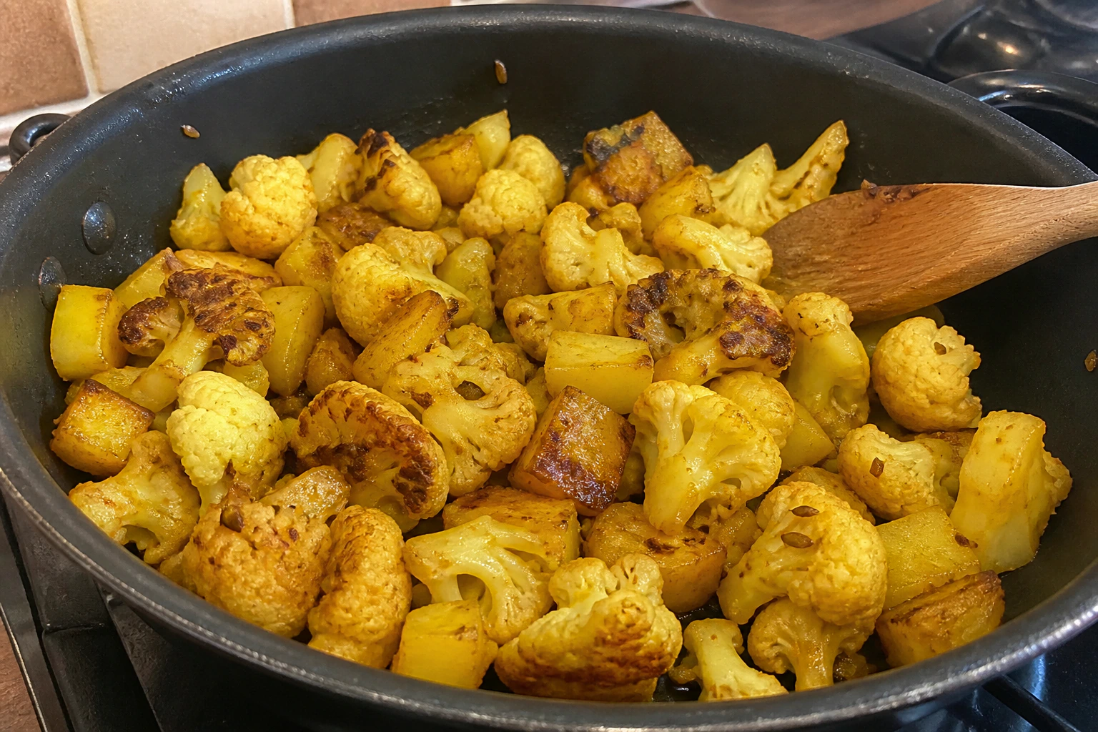Potato and cauliflower frying in one layer with lightly browned edges in a home kitchen pan