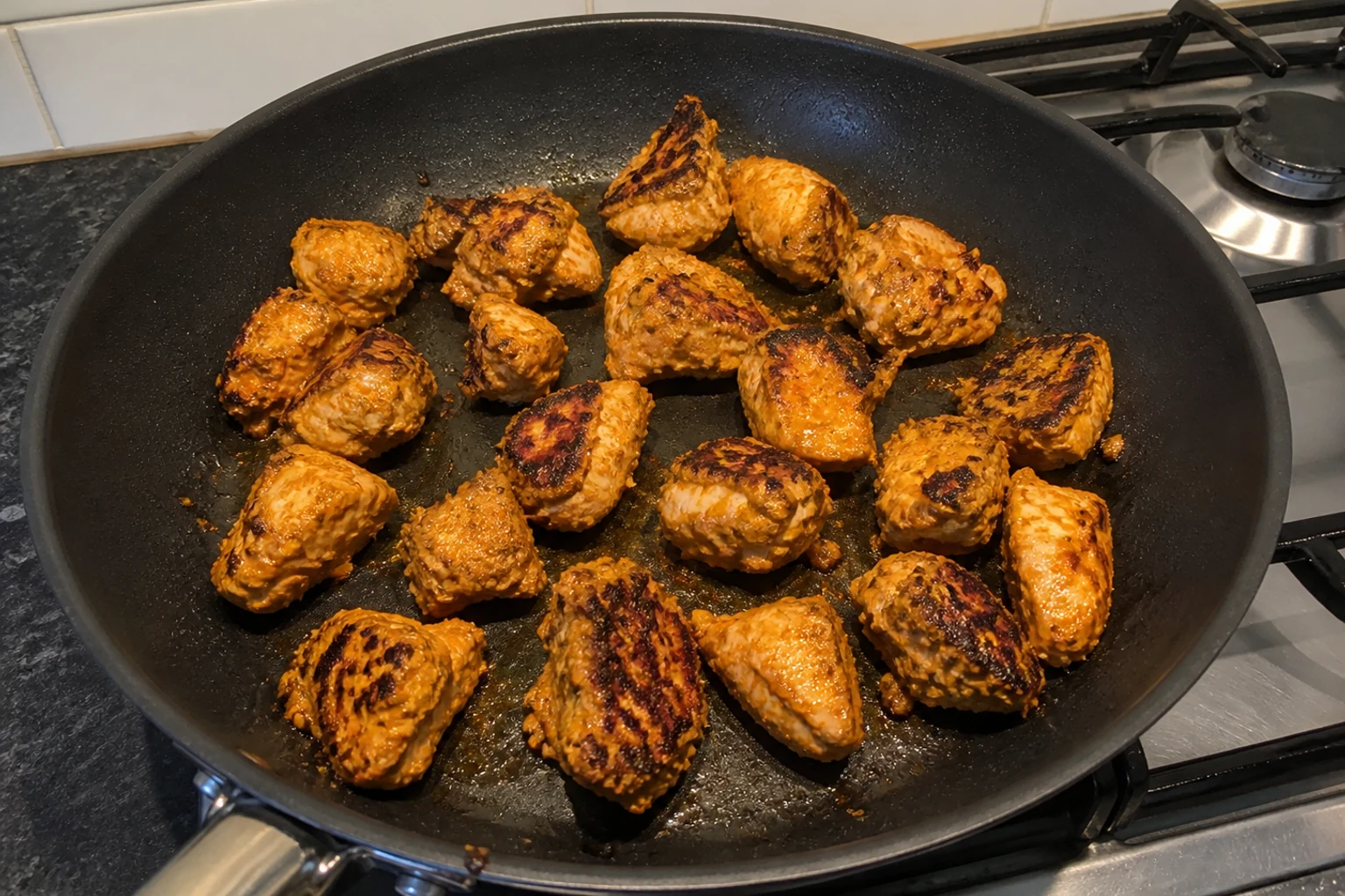 Yoghurt-marinated chicken pieces with charred patches cooking in a hot home kitchen frying pan