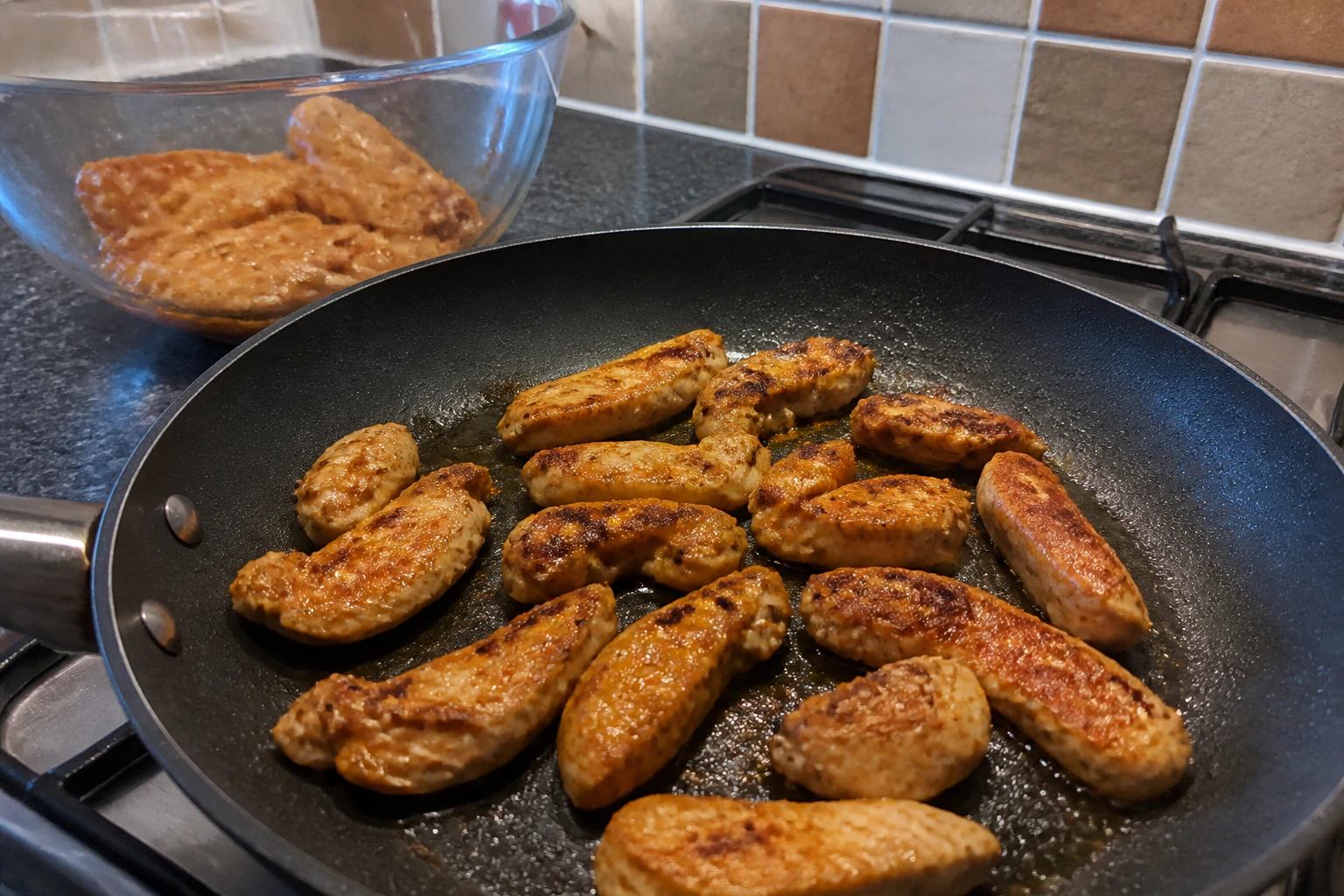 Yoghurt-marinated chicken pieces searing with space between them in a very hot home kitchen griddle pan