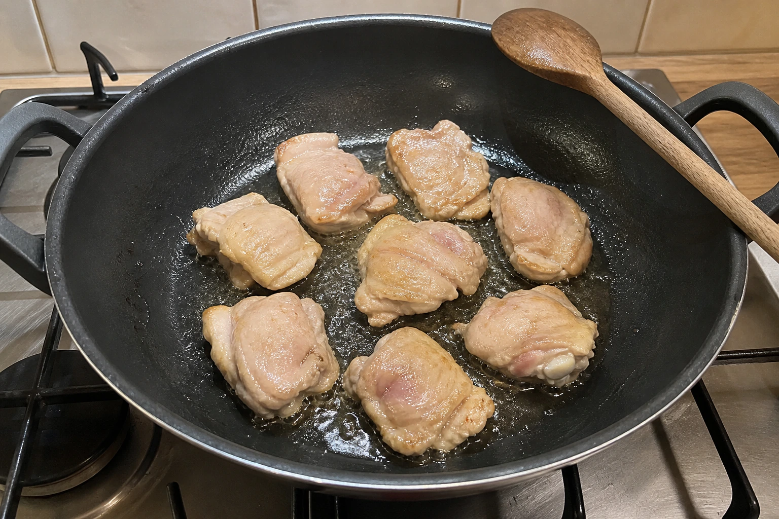 Boneless chicken pieces browning with generous space between them in a wide home kitchen pan