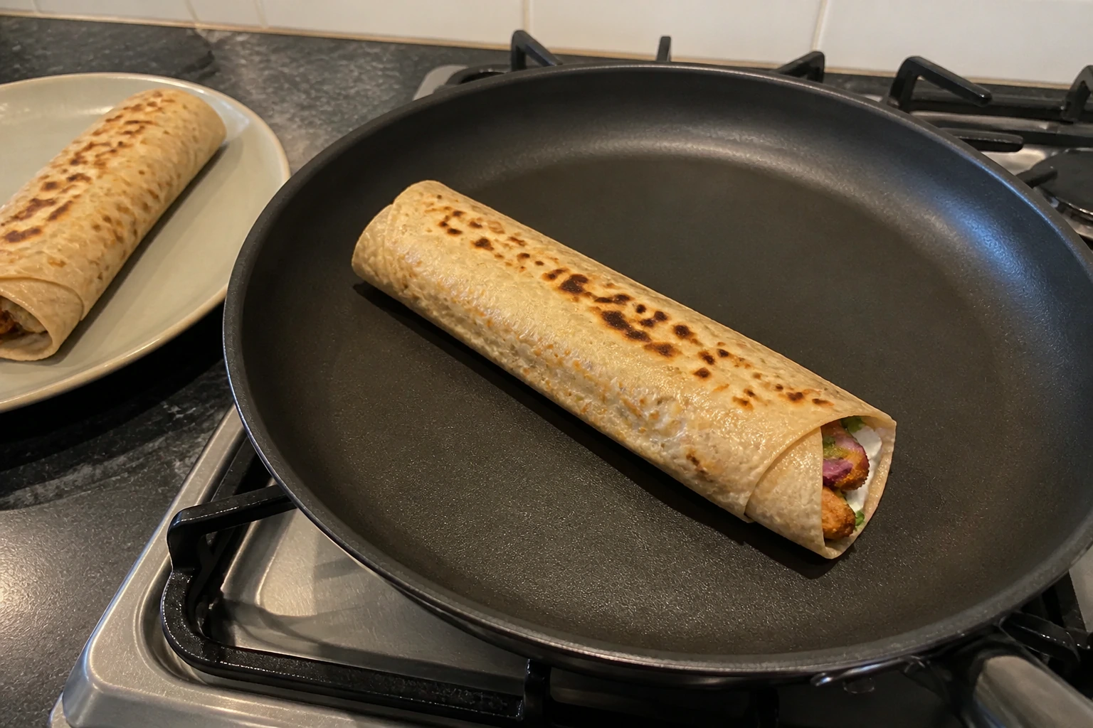 A filled chicken kathi roll resting seam-side down in a dry frying pan to seal closed