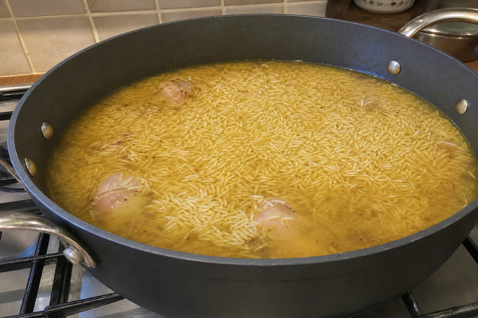 Flat layer of drained basmati rice in a heavy pot with hot stock sitting about one centimetre above it