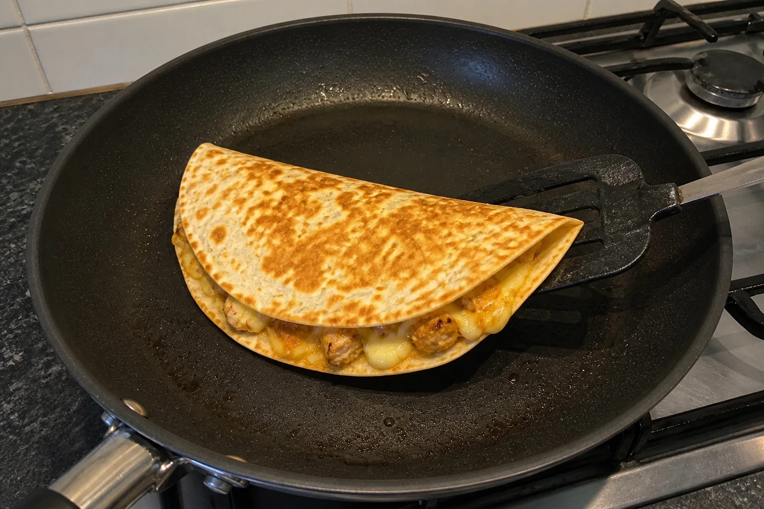 Golden folded chicken quesadilla lifted in a frying pan with melted cheese visible at the edge