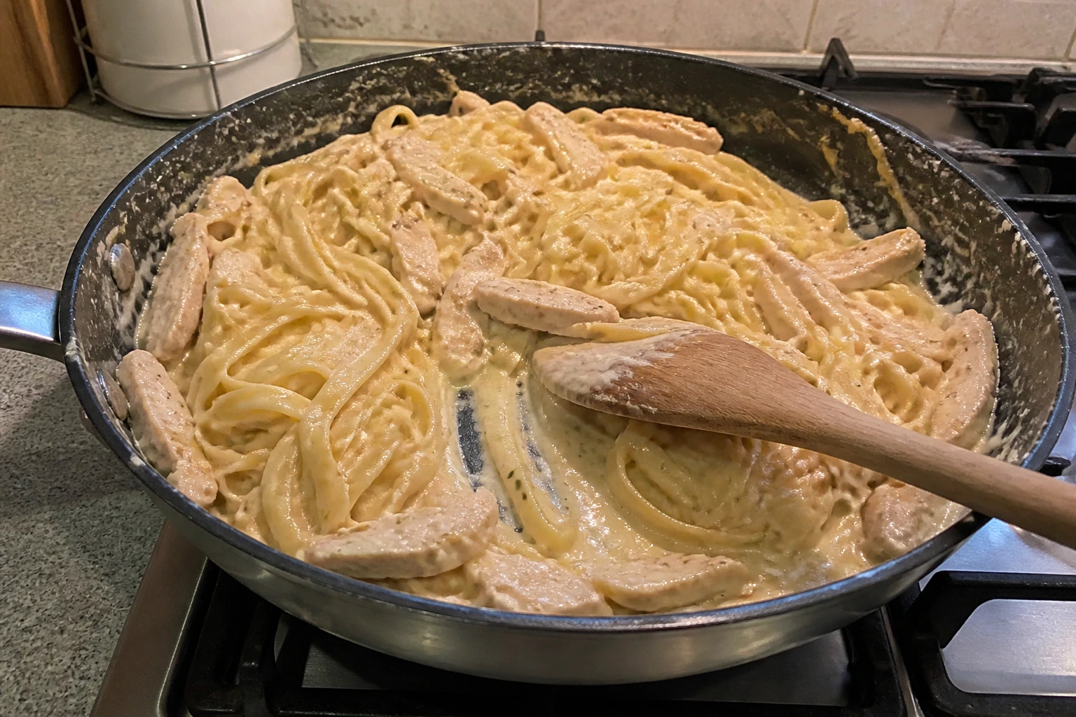 Creamy chicken pasta being tossed until a glossy sauce clings to every piece in a home kitchen pan