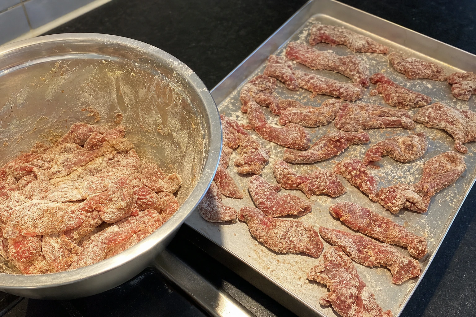 Thin beef strips separated and covered in a dry powdery cornflour coating in a kitchen bowl