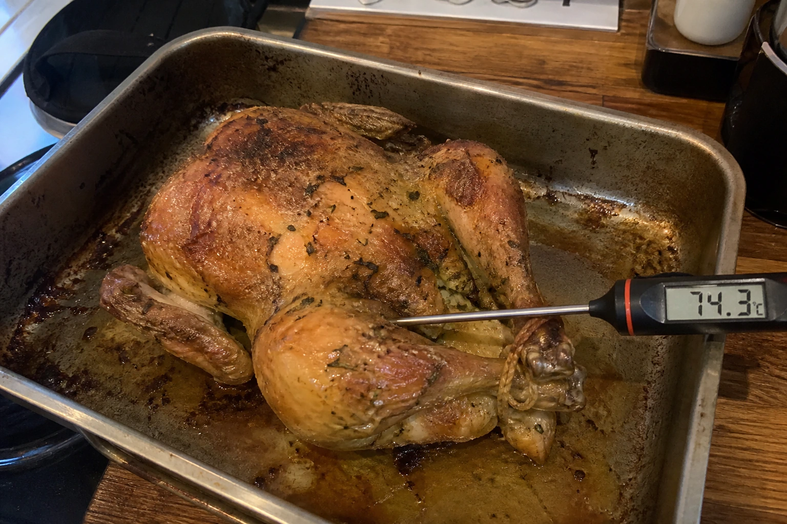 Imperfect home-roasted herb butter chicken in a used tin with a probe in the thickest thigh