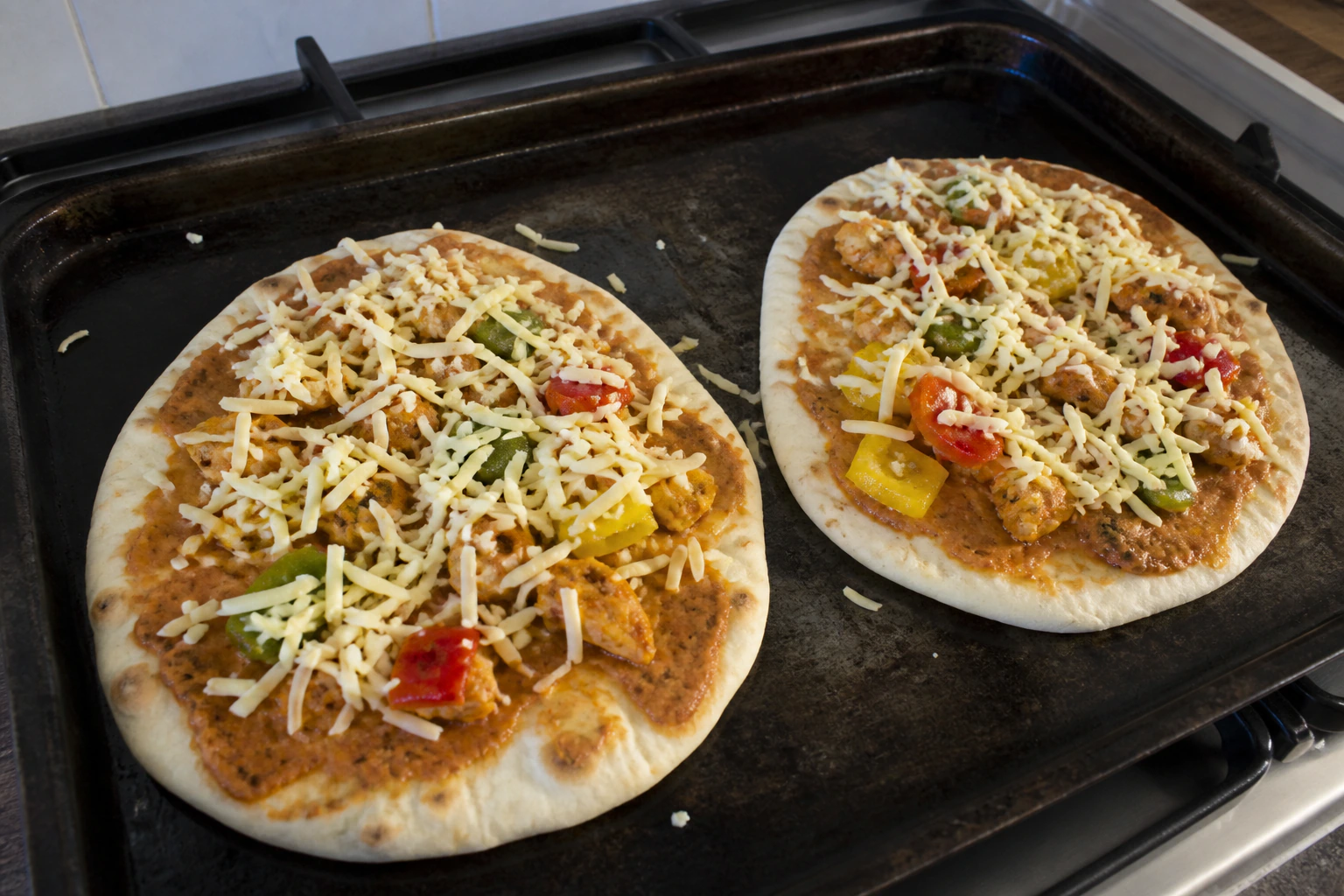 Two naan pizzas with a light even layer of mozzarella chicken peppers and onion before baking