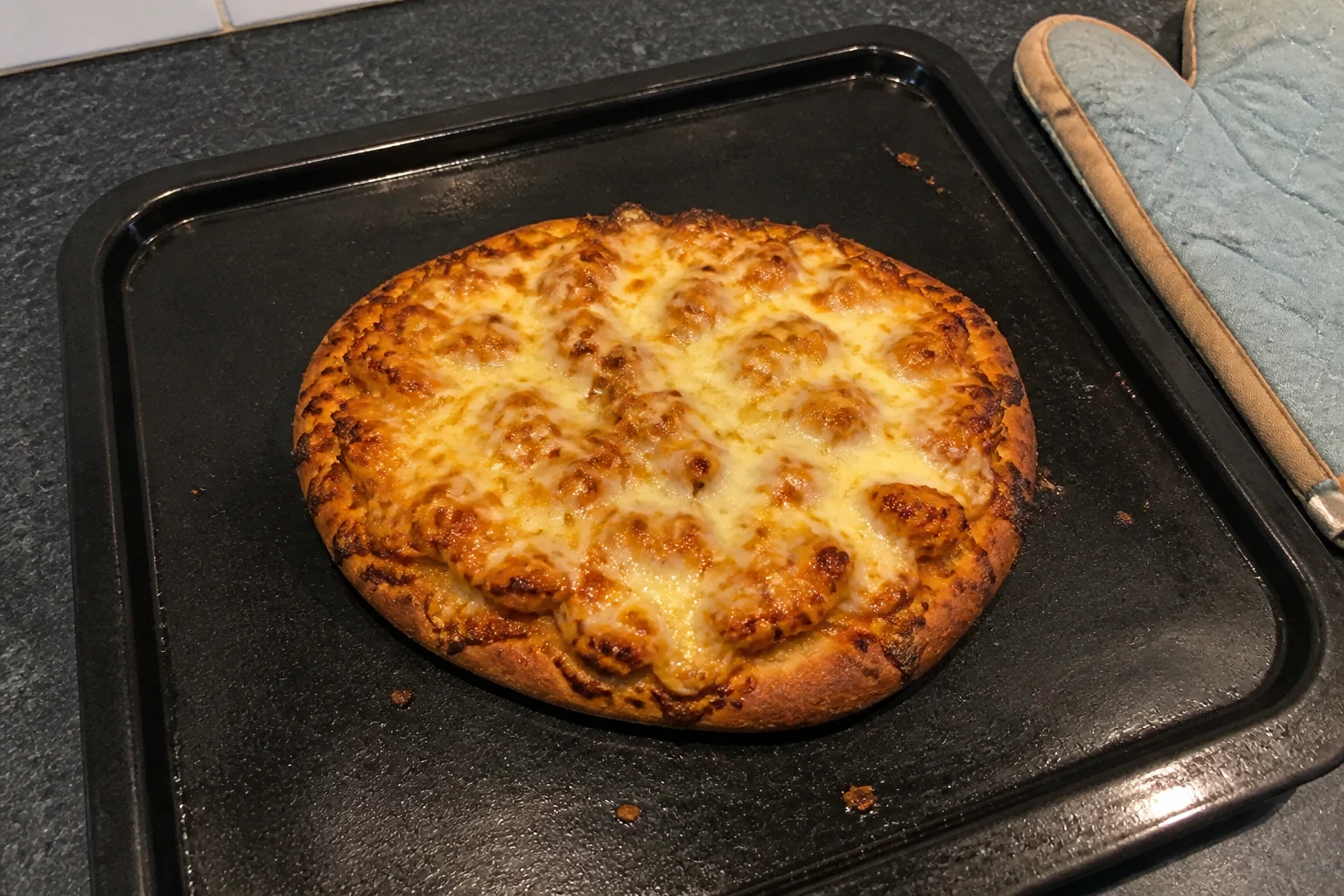 Masala naan pizza on an oven tray with crisp darkened edges and bubbling golden cheese