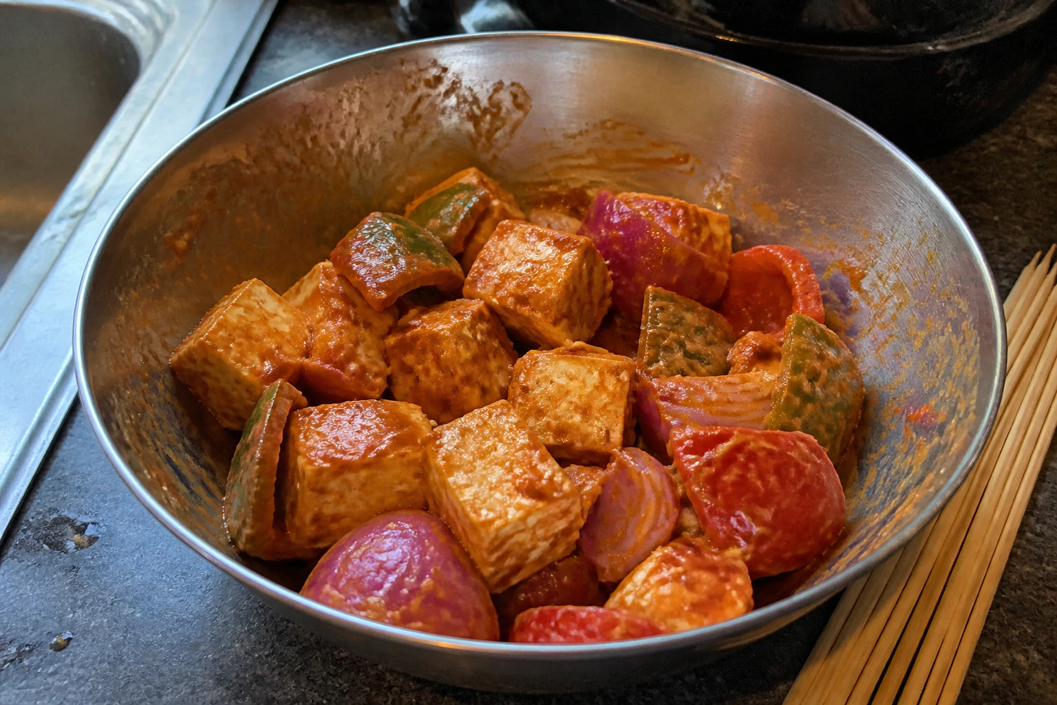 Firm uneven paneer cubes onion and pepper resting briefly in yoghurt masala beside bamboo skewers