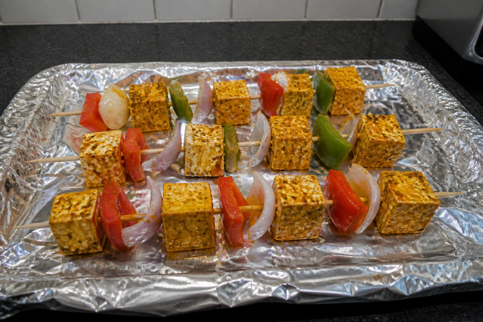 Paneer pepper and onion threaded onto skewers with small even gaps on a kitchen tray