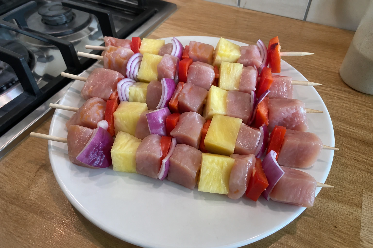 Chicken pineapple red pepper and onion alternated on skewers with small even gaps on a kitchen tray