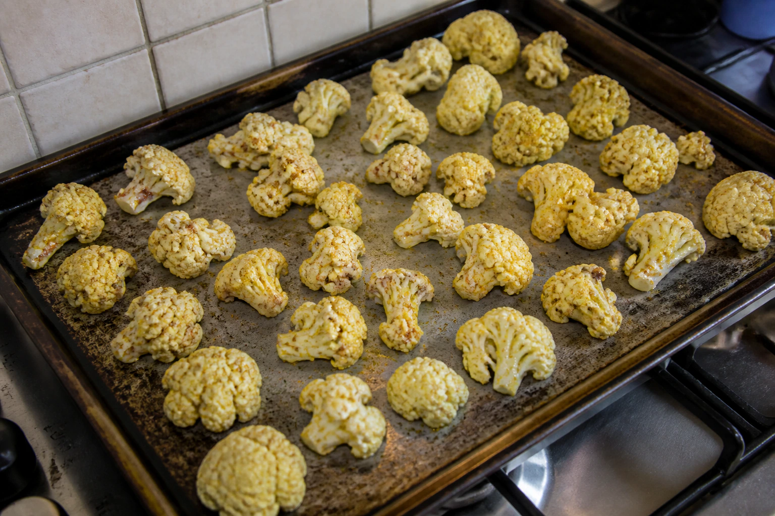 Seasoned cauliflower florets spread with visible space between them across a large roasting tray