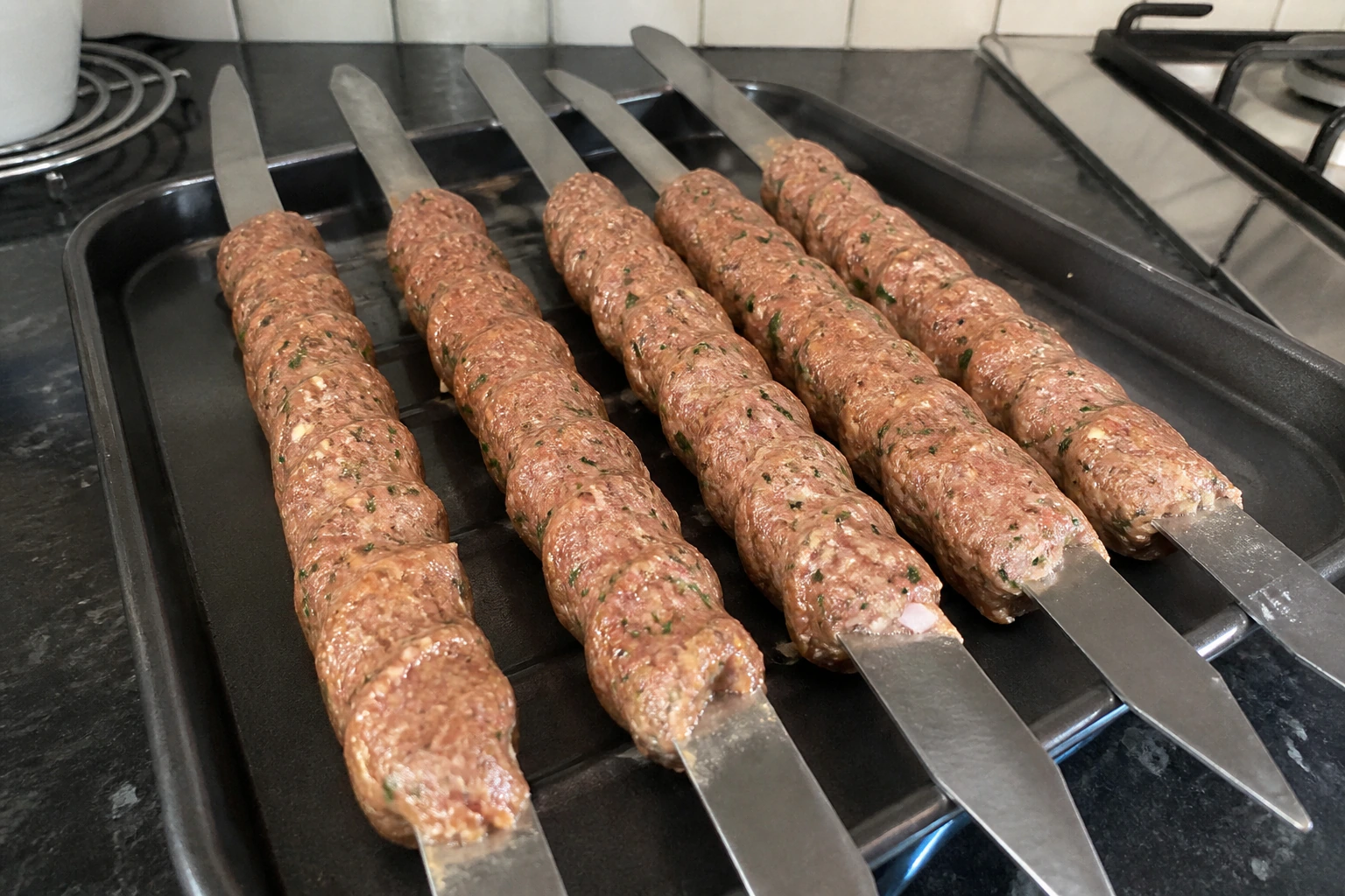 Evenly shaped seekh kebabs pressed around metal skewers and arranged on a tray before cooking