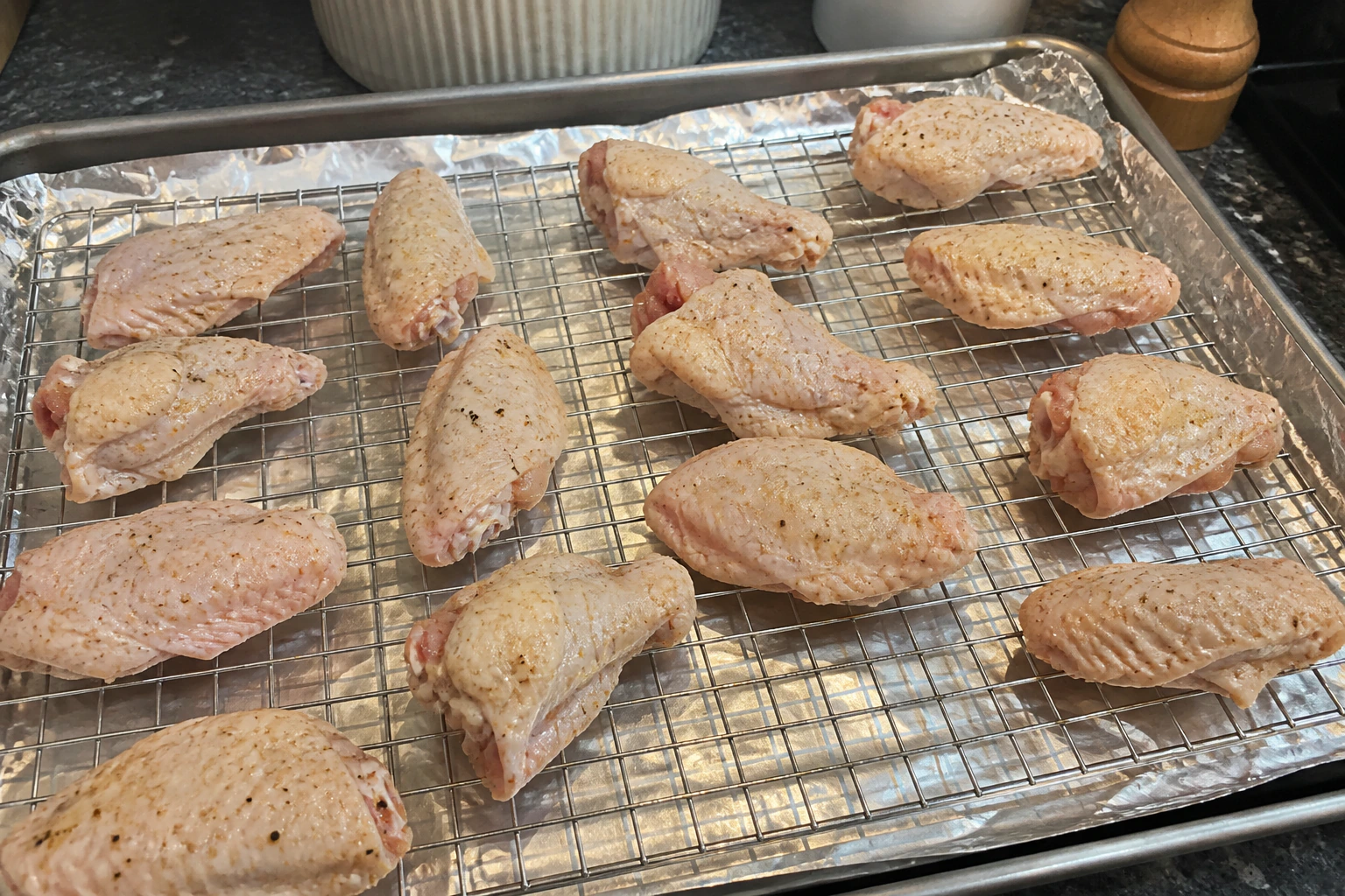 Dry seasoned chicken wings spaced apart skin-side up on a wire rack over a lined oven tray