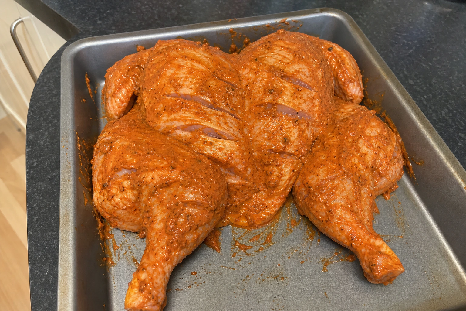 Whole chicken with shallow cuts covered in a thick red-orange tandoori yoghurt marinade that clings without pooling
