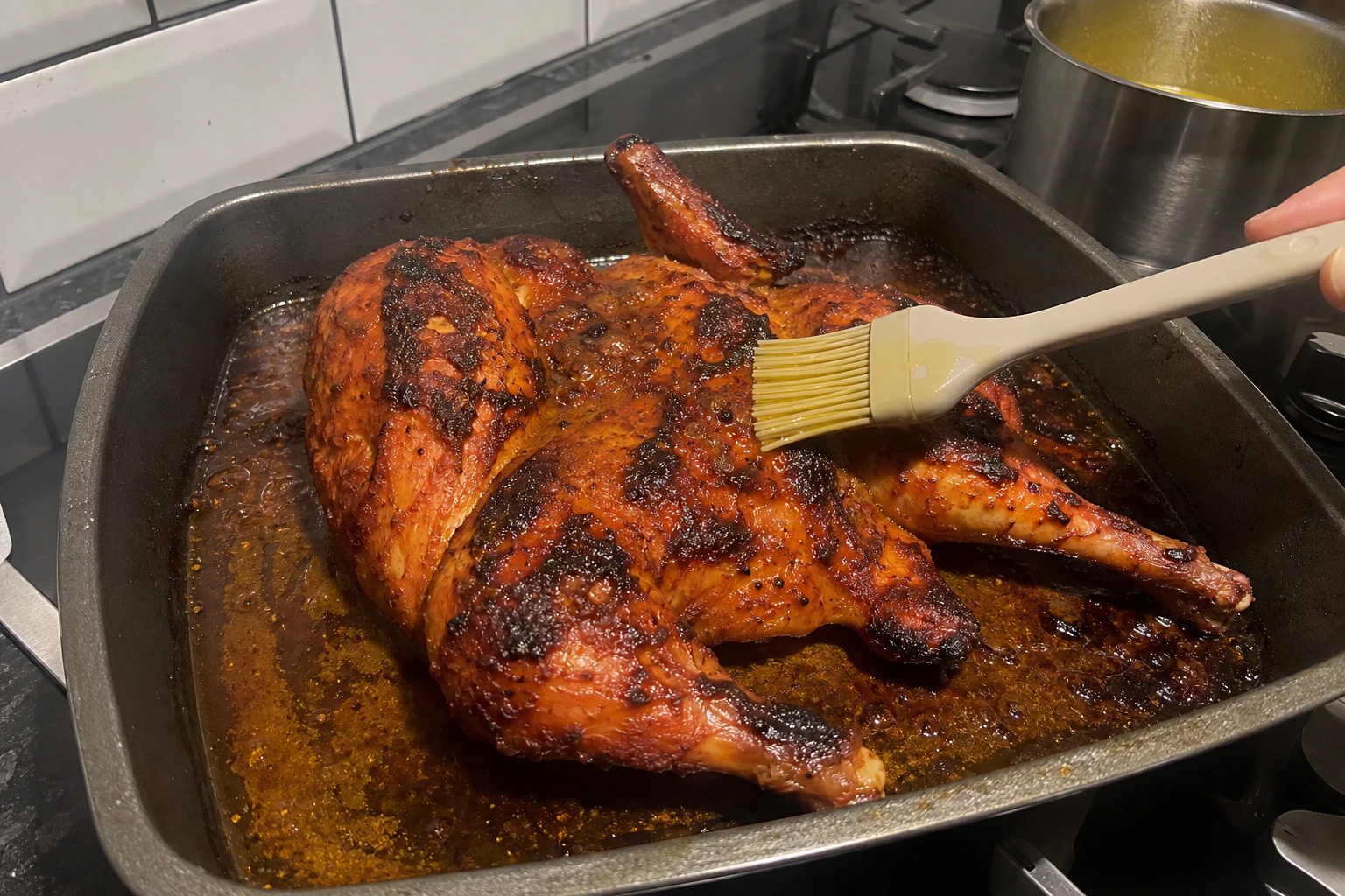 Nearly roasted tandoori chicken being brushed with melted butter in a home kitchen roasting tray