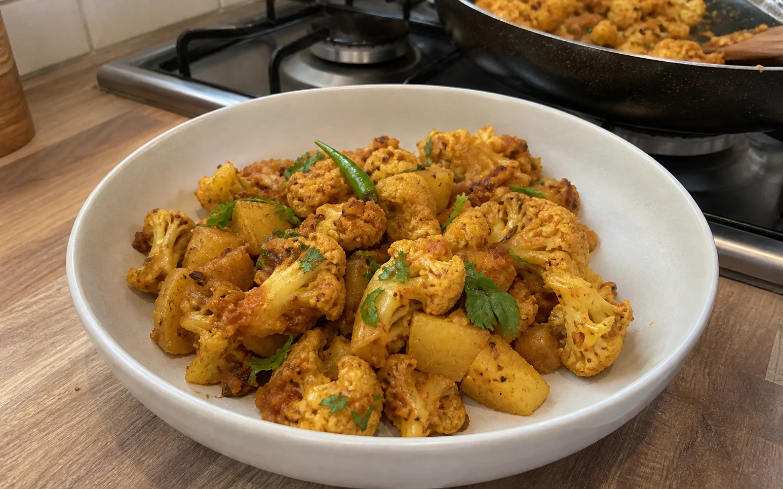 Homemade aloo gobi with browned cauliflower and potato in a dry golden masala beside the hob