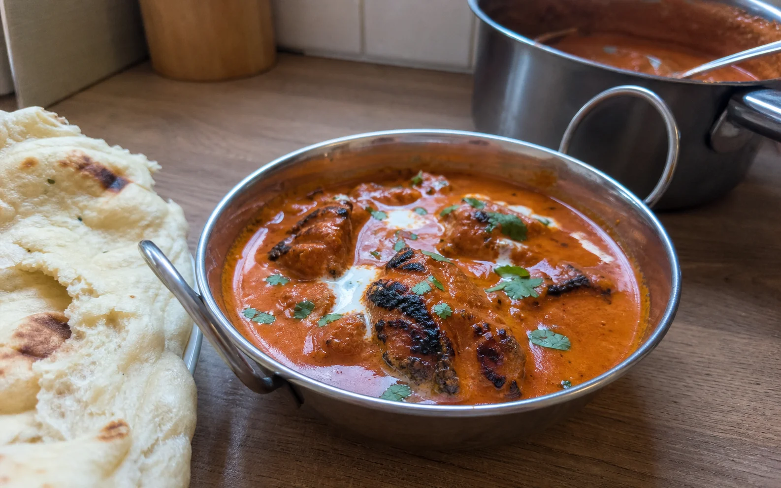 Homemade butter chicken with charred chicken pieces in a creamy tomato sauce beside naan