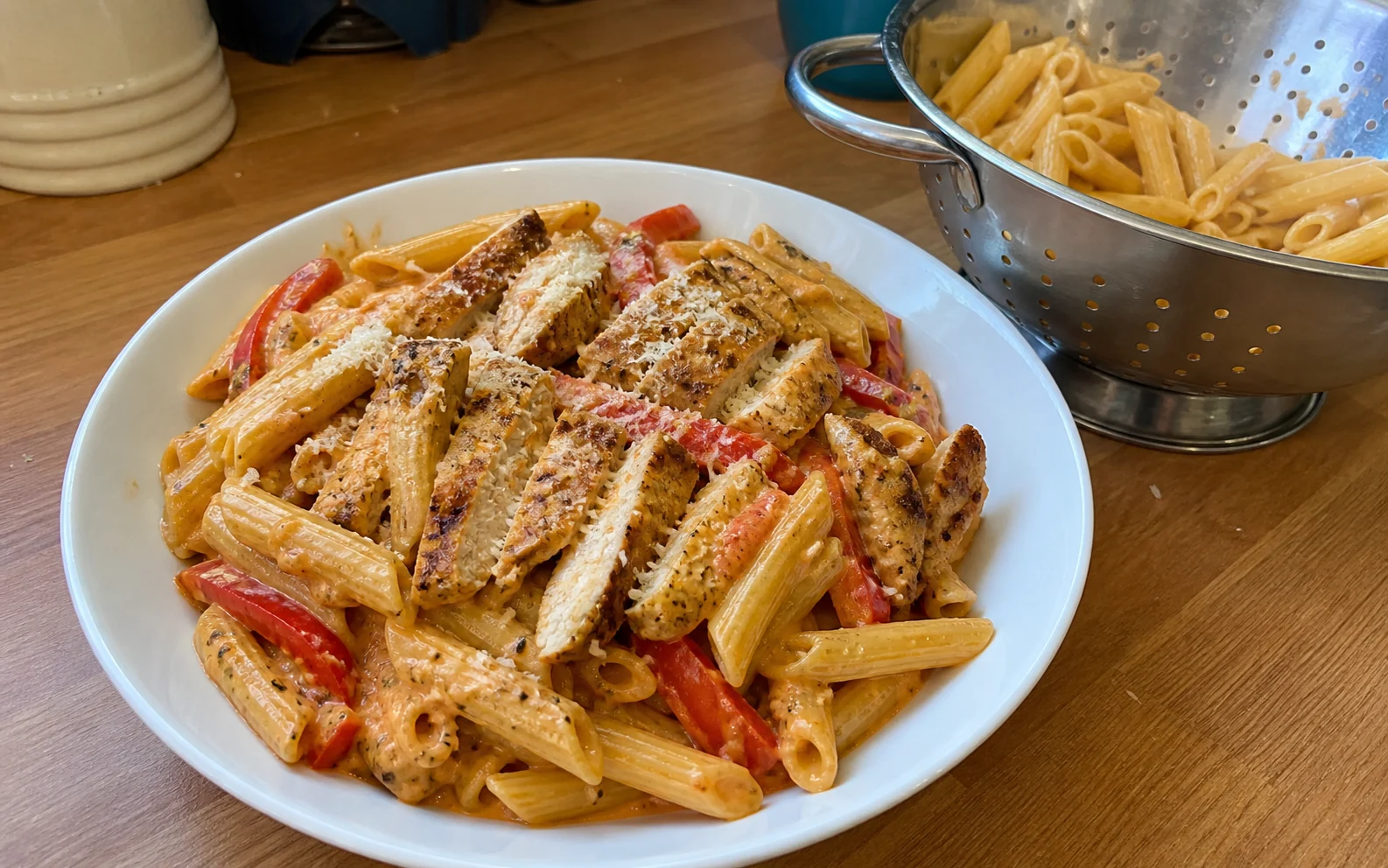 Creamy Cajun-style chicken pasta with red pepper in an everyday bowl beside the colander