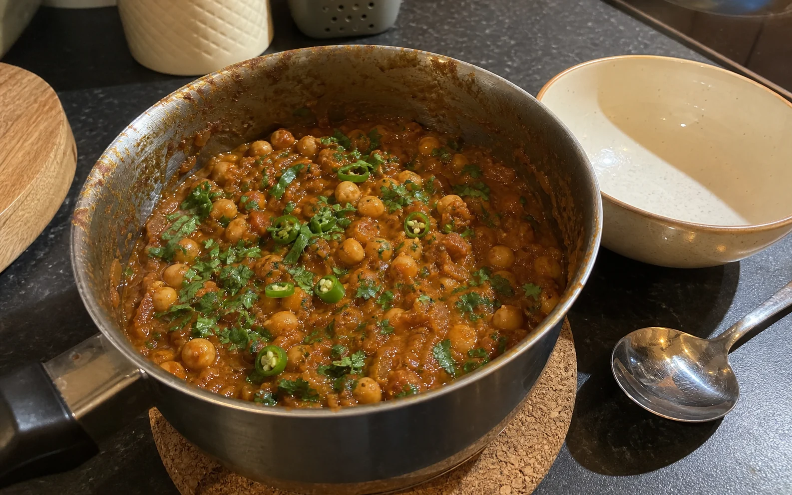 Thick homemade chana masala finished with coriander and green chilli in a well-used saucepan