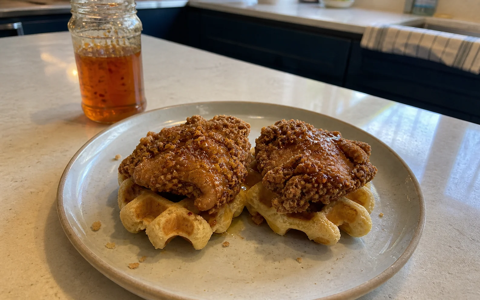 Craggy fried chicken on two waffles with a light hot honey drizzle on a kitchen island