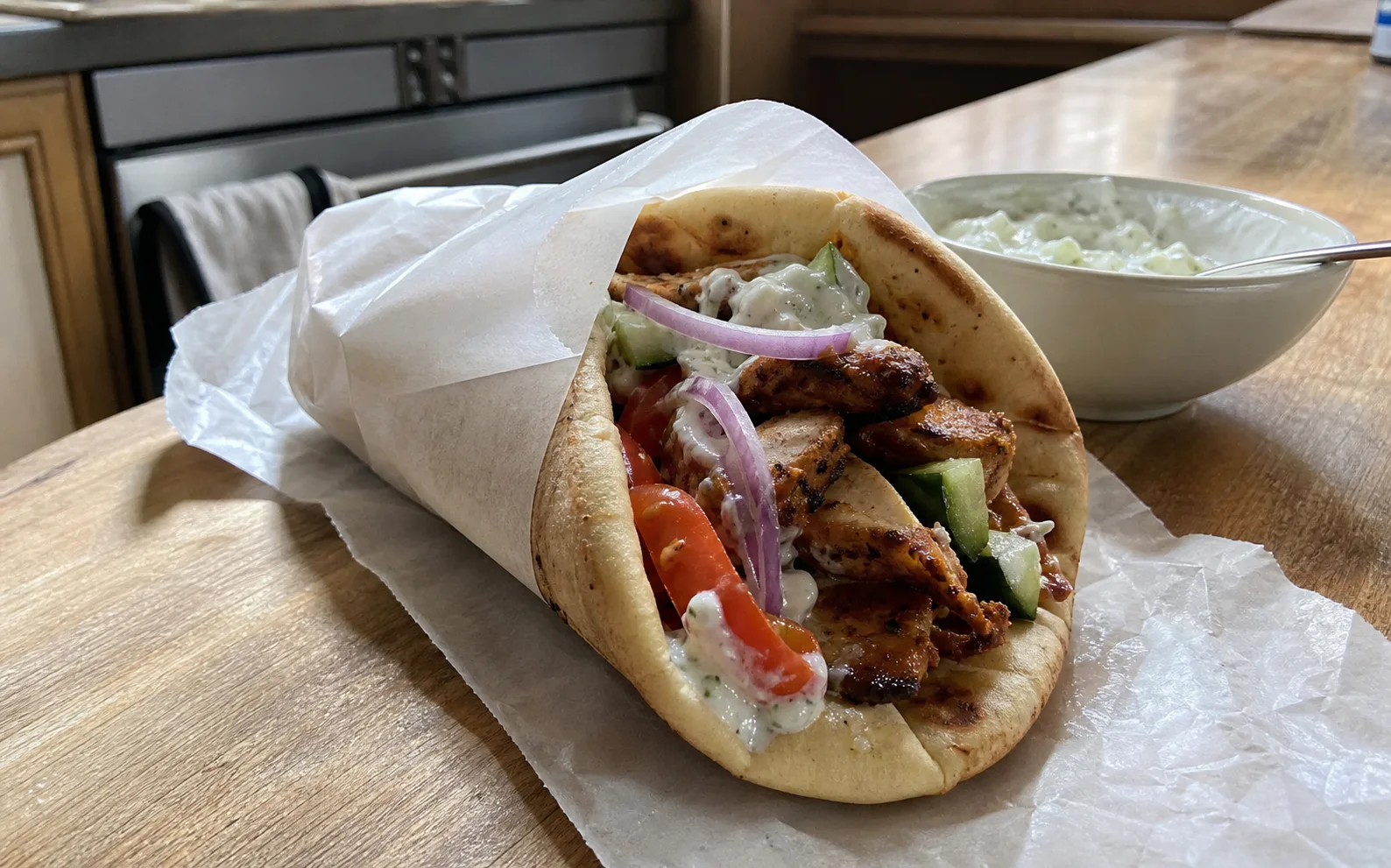 Homemade chicken gyros in warm flatbread with tomato, cucumber, red onion and tzatziki on a kitchen table