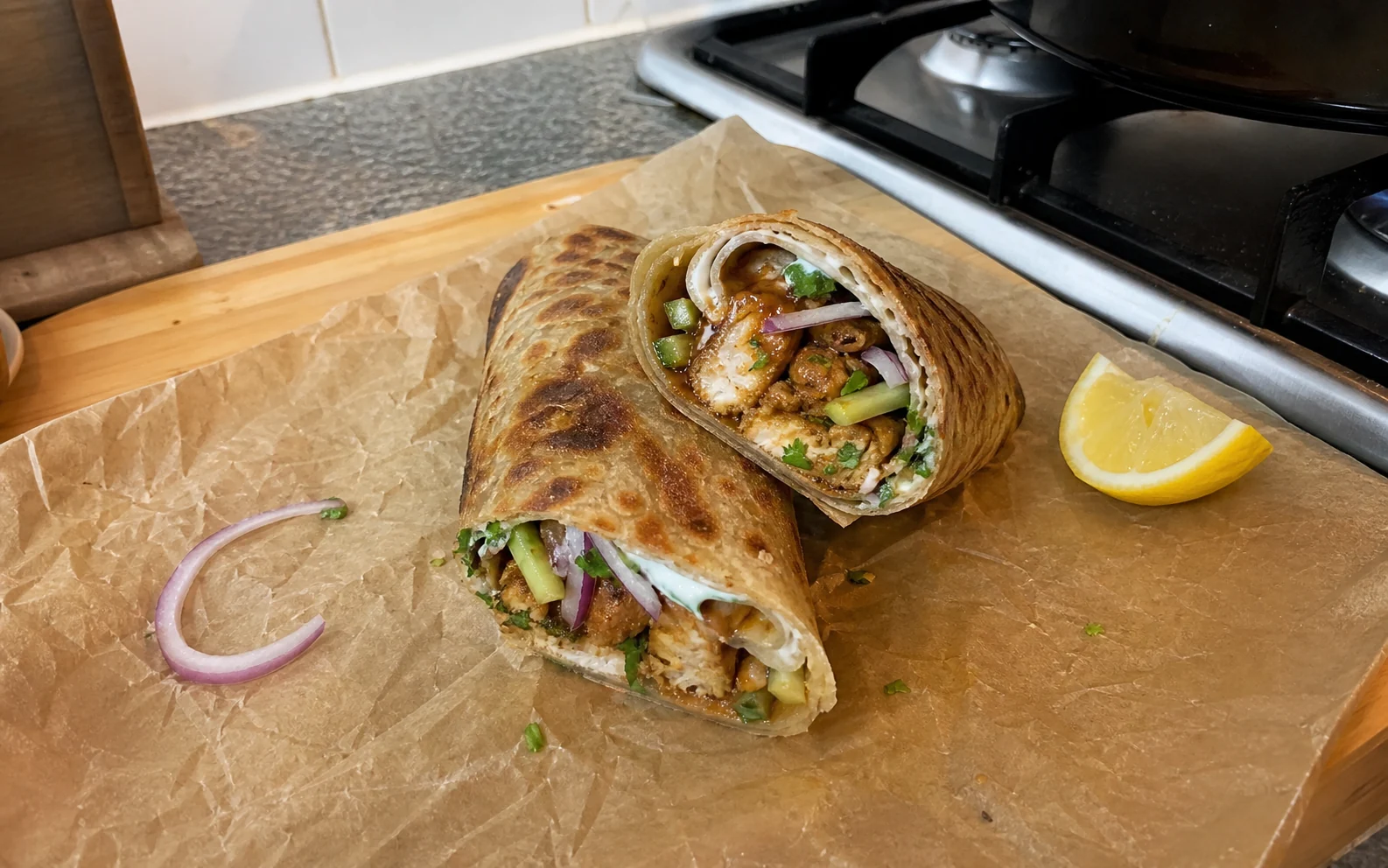 Chicken kathi rolls cut open to show masala chicken, cucumber, onion and mint yoghurt
