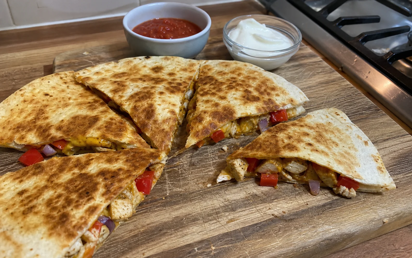 Browned chicken quesadilla wedges with pepper, onion and melted cheese on a wooden board