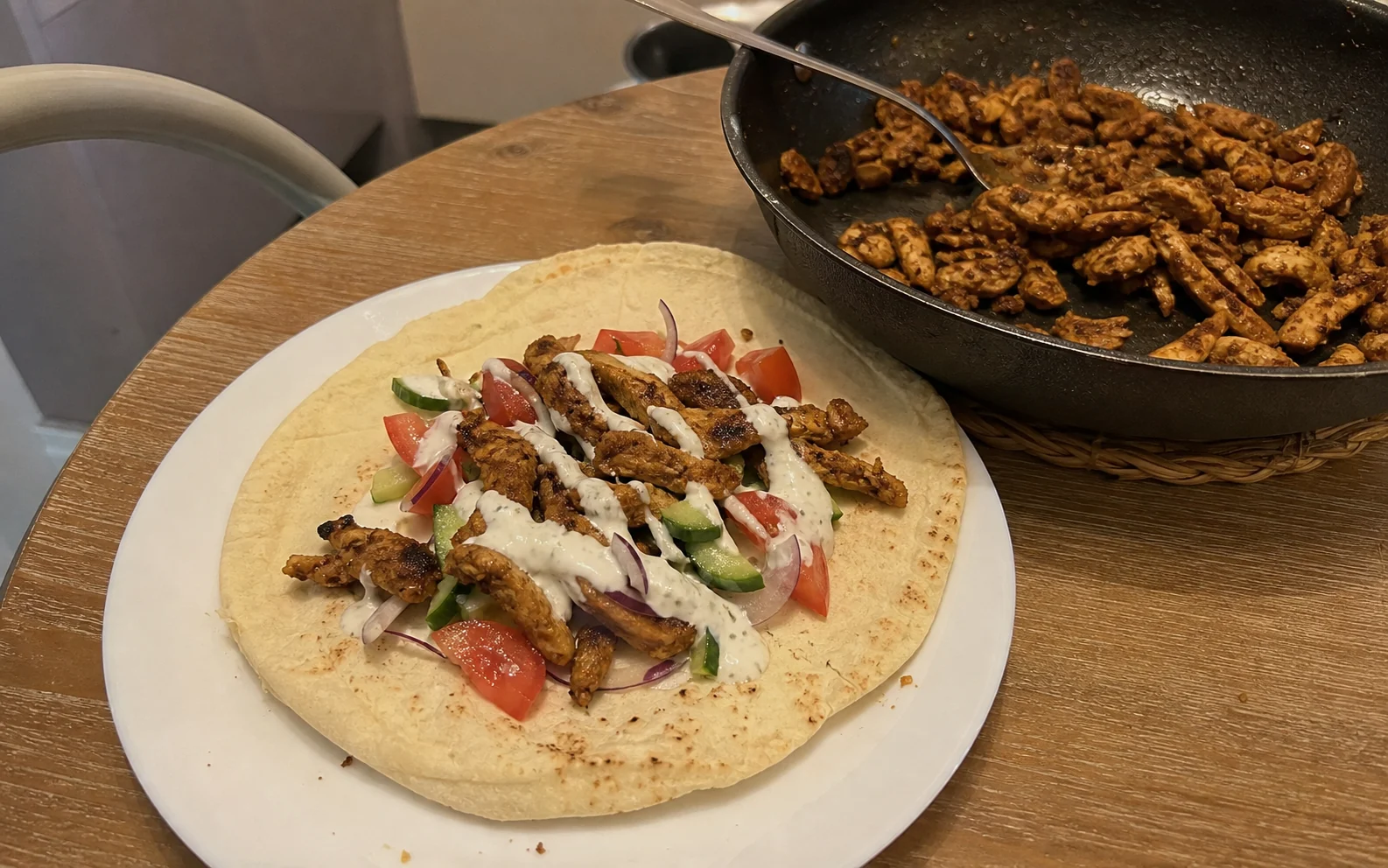 Open chicken shawarma flatbread with caramelised chicken, salad and garlic sauce beside the frying pan