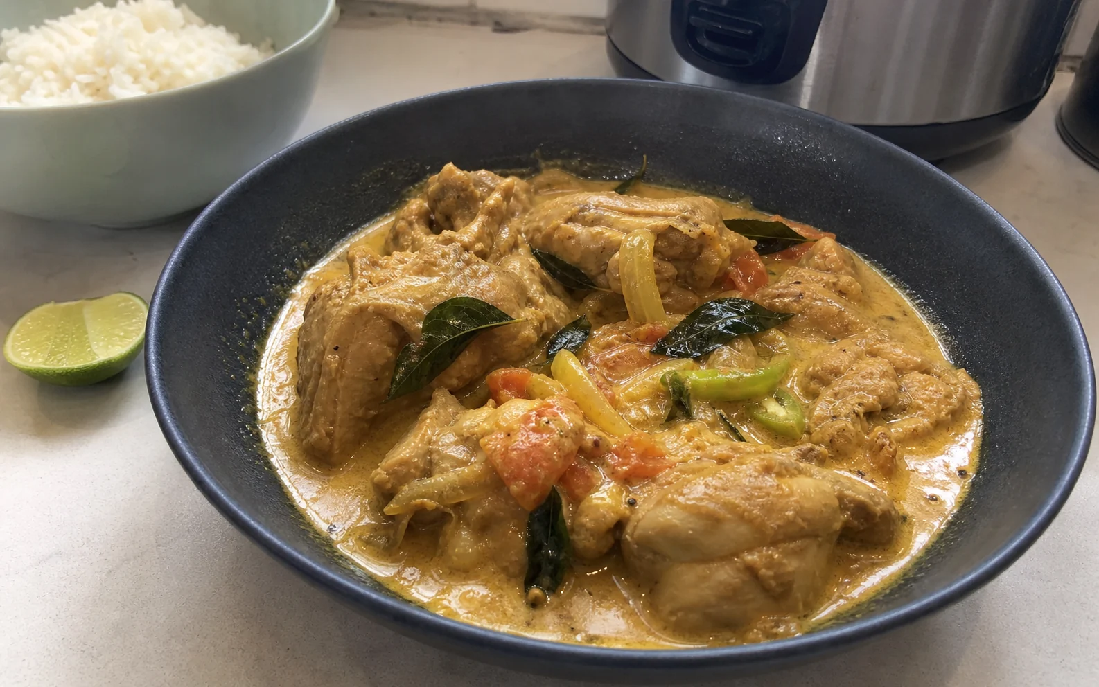 Sri Lankan-inspired coconut chicken curry with curry leaves, tomato and green chilli beside rice