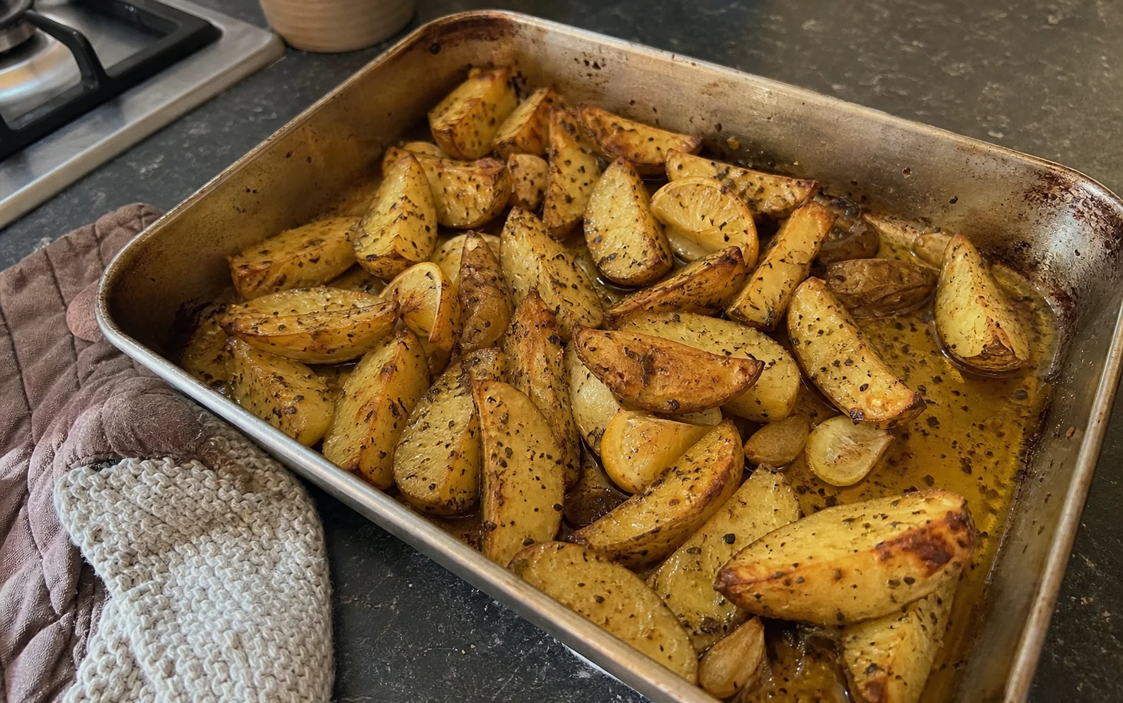 Greek-style lemon roast potato wedges with oregano and garlic in a used roasting tin