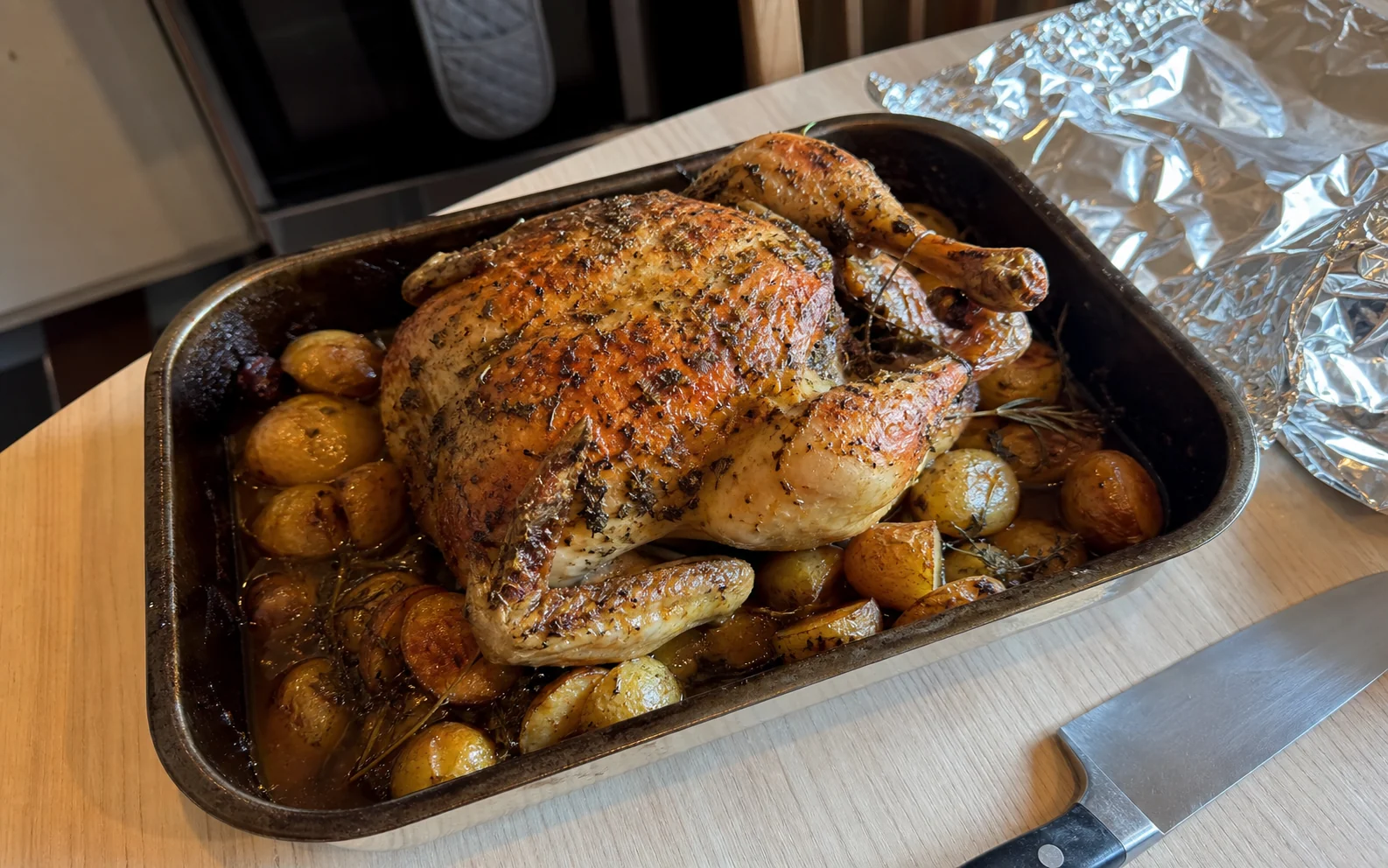 Whole herb-butter roast chicken with baby potatoes and pan juices in its roasting tin