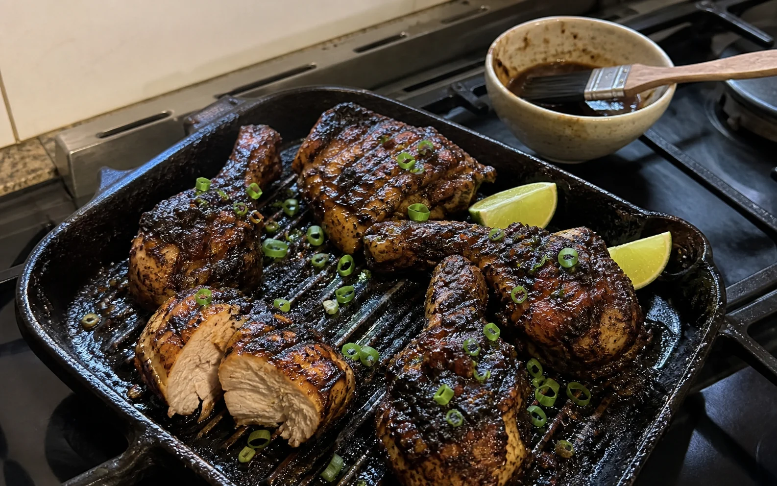 Charred homemade jerk chicken thighs and drumsticks in a ridged pan on the hob