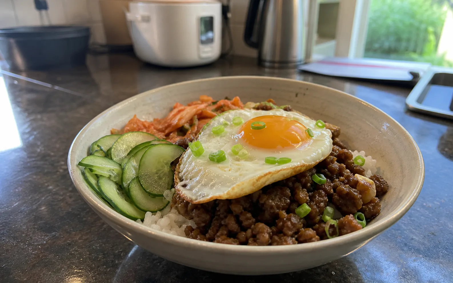 Korean-inspired beef rice bowl with cucumber, kimchi and a fried egg on a home kitchen counter