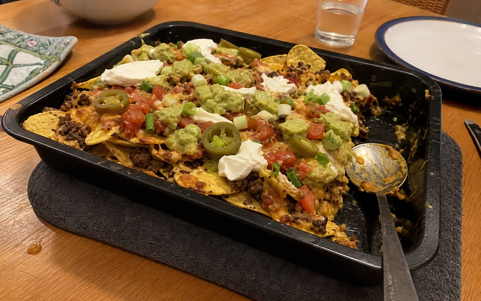 Homemade loaded beef nachos with melted cheese, salsa, guacamole and sour cream in a baking tray