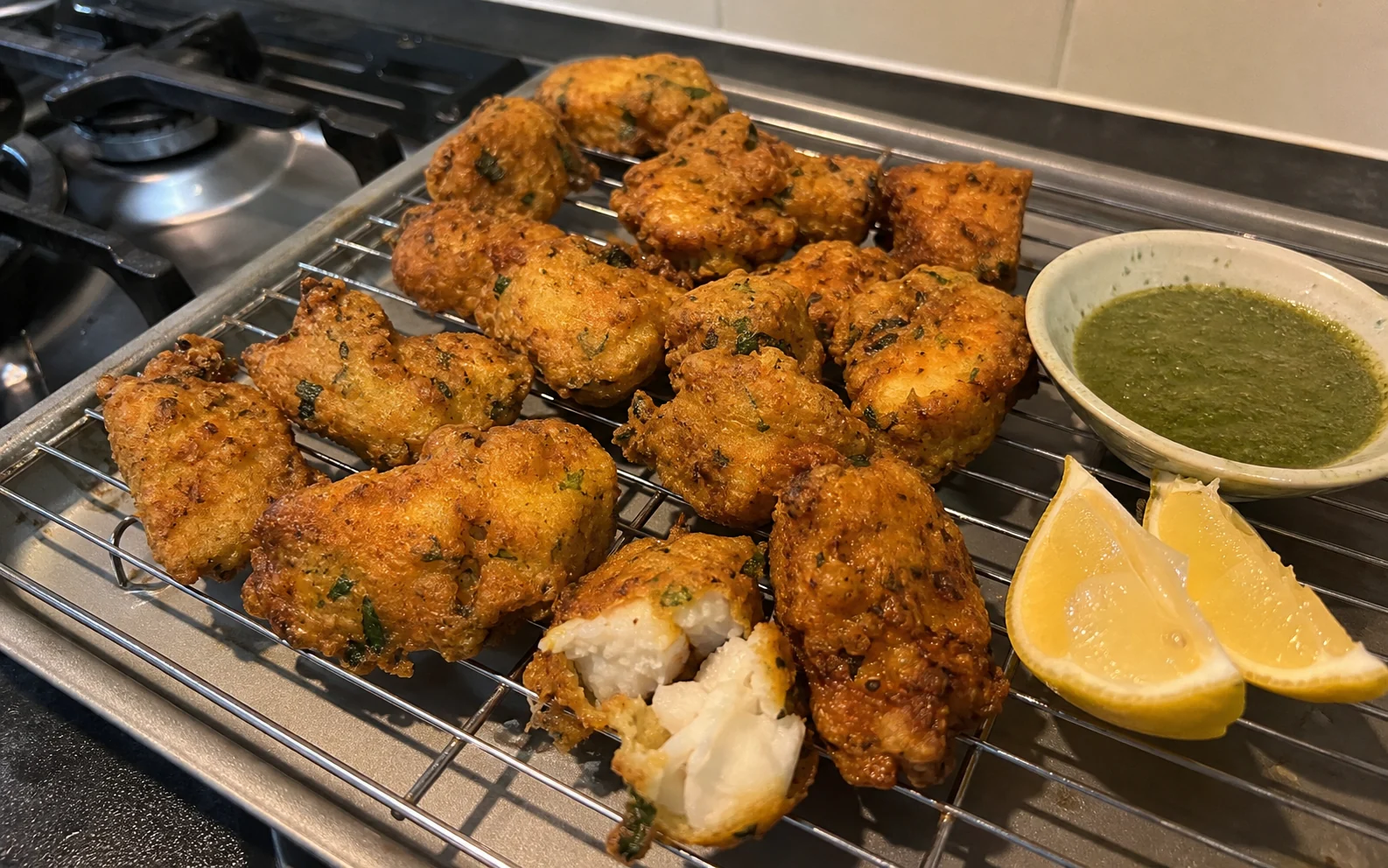 Crisp masala fish pakoras draining on a wire rack with flaky white fish visible