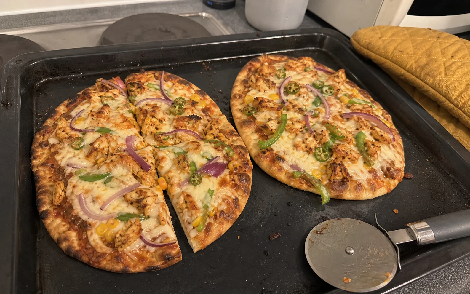 Two masala naan pizzas with chicken, mozzarella, onion, green pepper and chilli on a baking tray