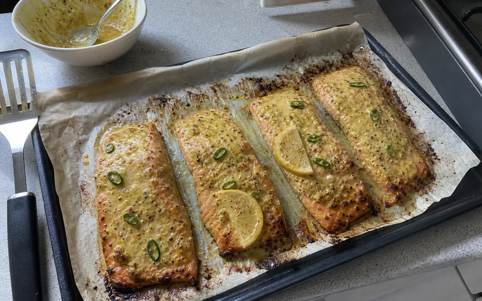 Mustard yoghurt glazed salmon fillets with green chilli and lemon on a parchment-lined tray
