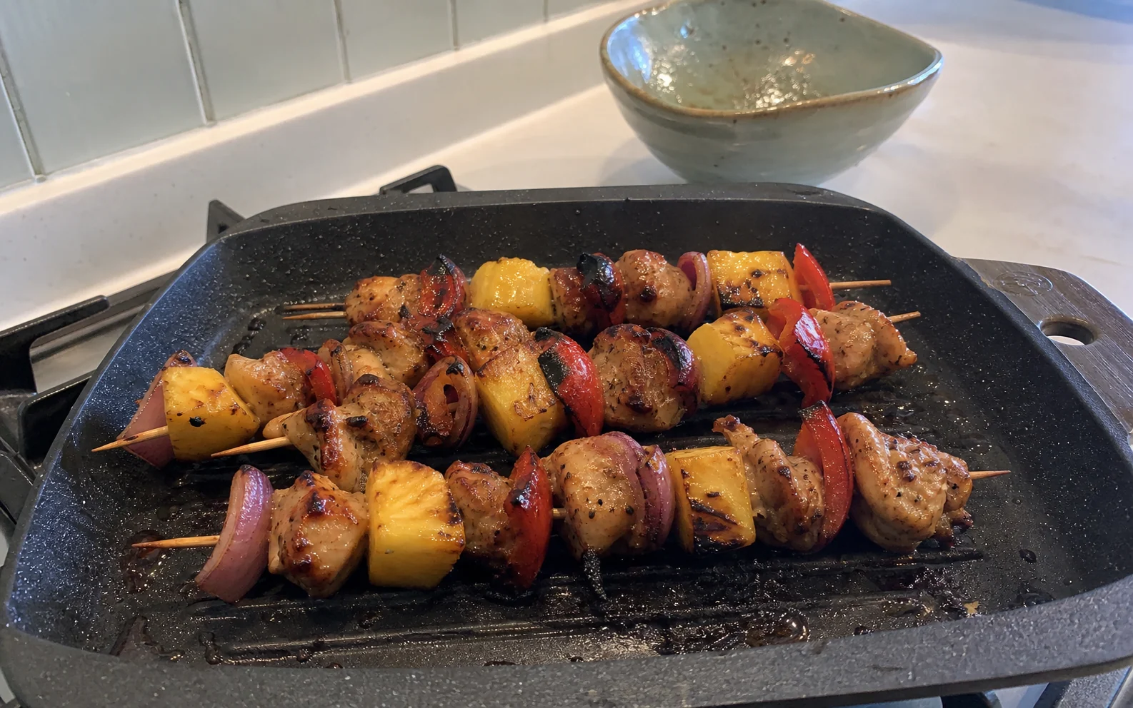 Pineapple chicken skewers with red pepper and onion cooking in a grill pan