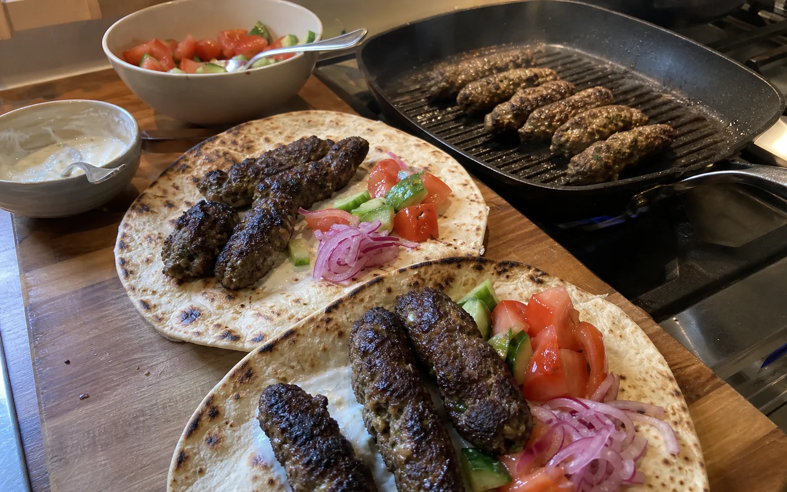 Hand-shaped seekh kebabs in flatbreads with salad, pickled onion and garlic yoghurt