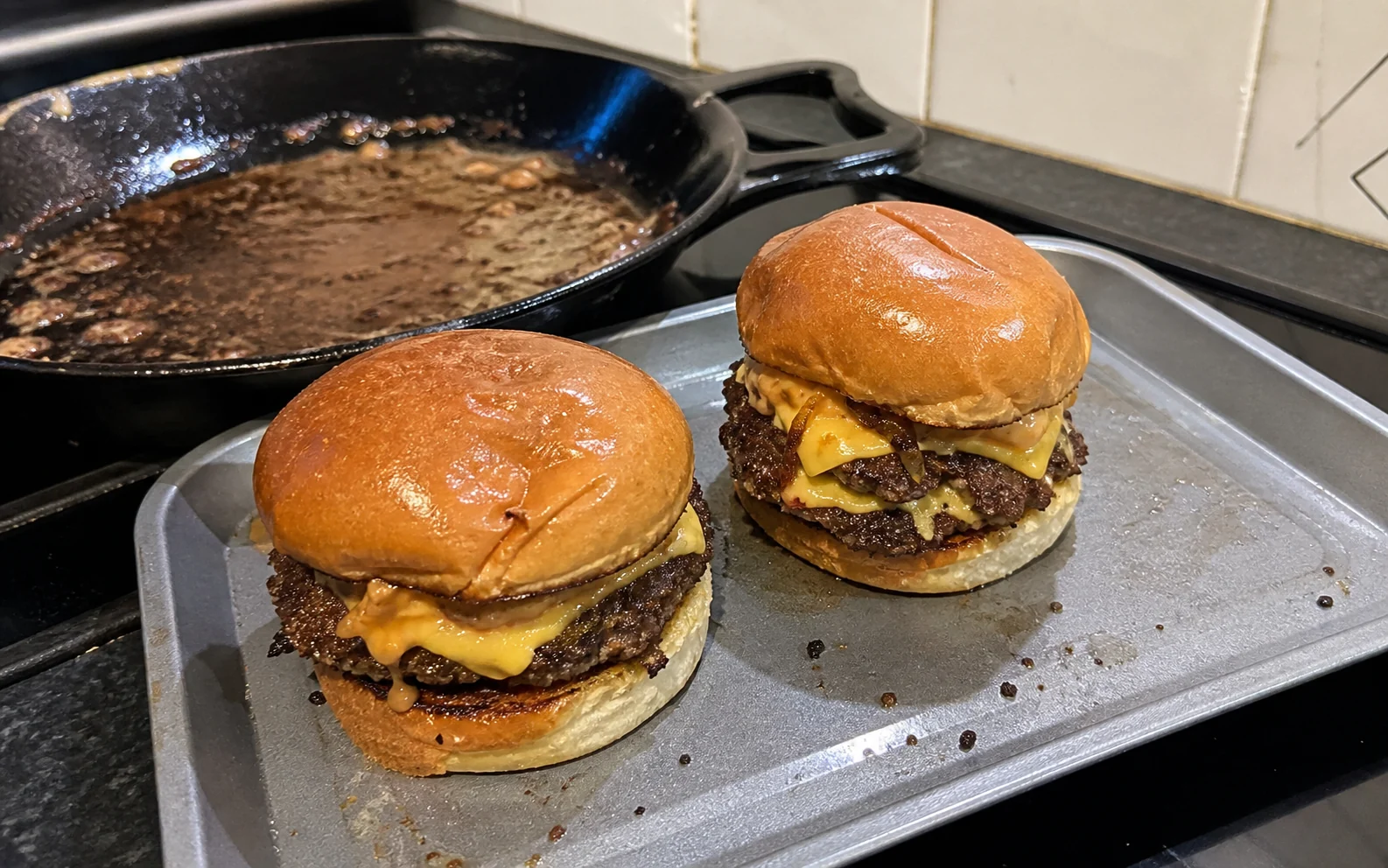 Two double smash burgers with melted cheese and masala sauce beside the cast-iron pan