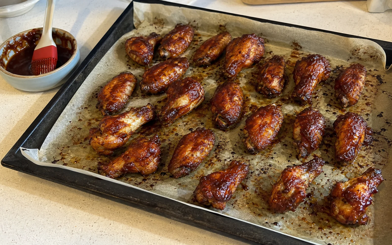 Baked sticky barbecue wings with caramelised edges on a parchment-lined sheet pan